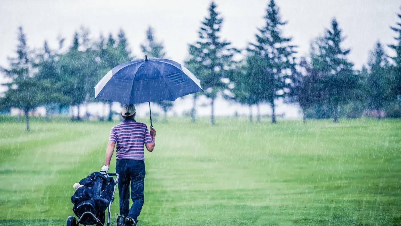 Golfare går i regn med bästa golfparaplyet över bagvagnen