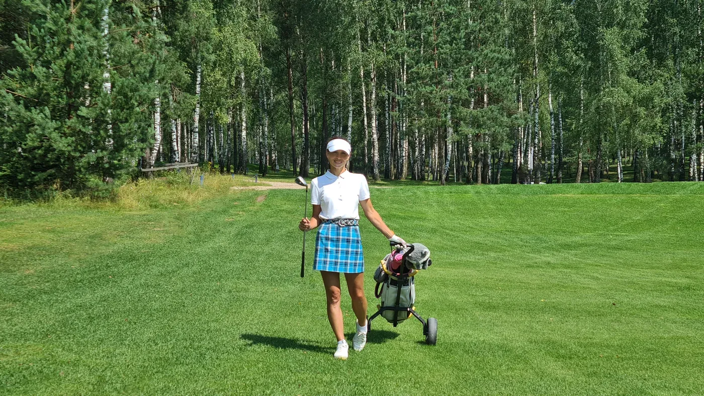 Kvinna drar bästa golfvagn med bag över fairway bland björkar