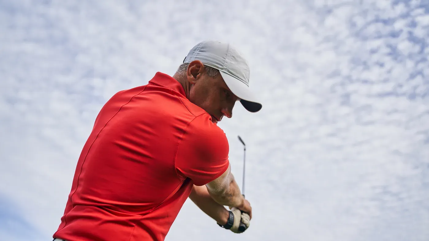 Golfare i närbild mitt i svingen mot molnig himmel